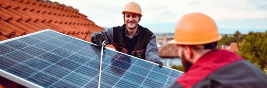 Two technicians install a solar planel on a tile rooftop